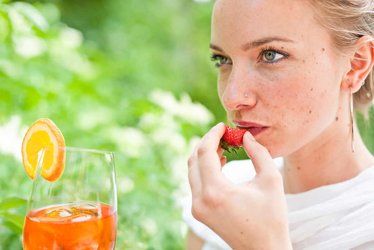 Signora che mangia fragole con un aperitivo in mano