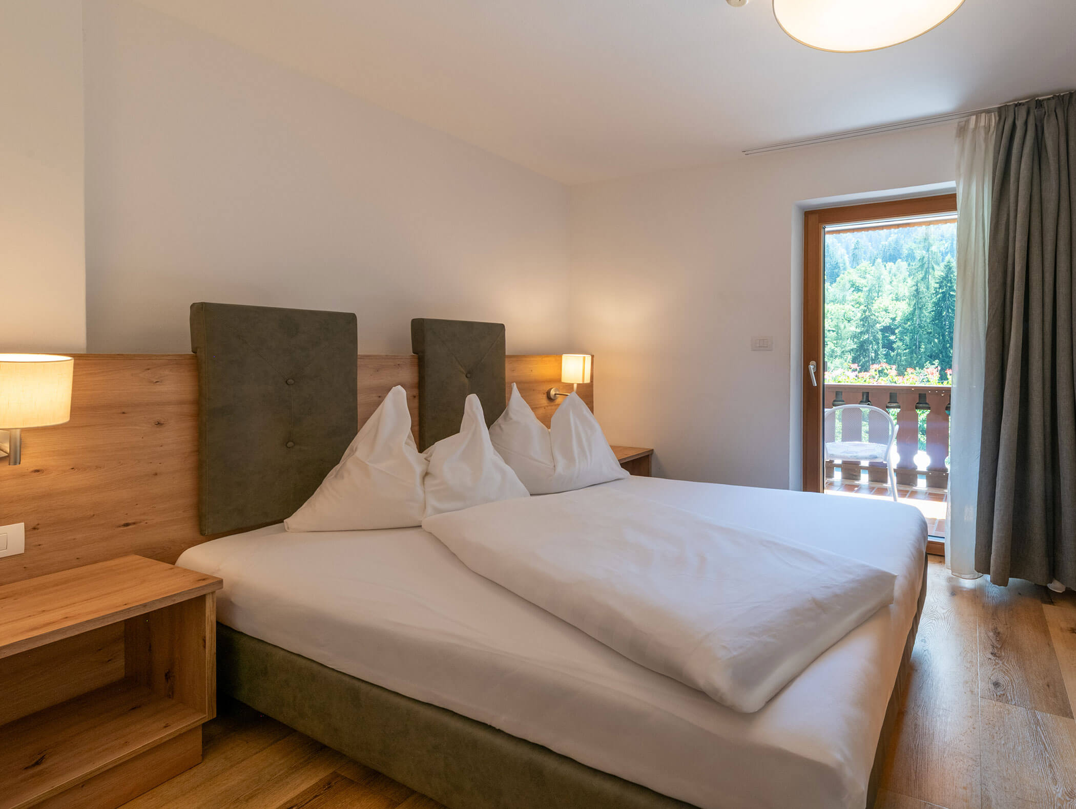 Camera d'albergo luminosa con letto matrimoniale, pavimento in legno, comodini e balcone con vista sugli alberi all'esterno. - Hotel Zur Sonne
