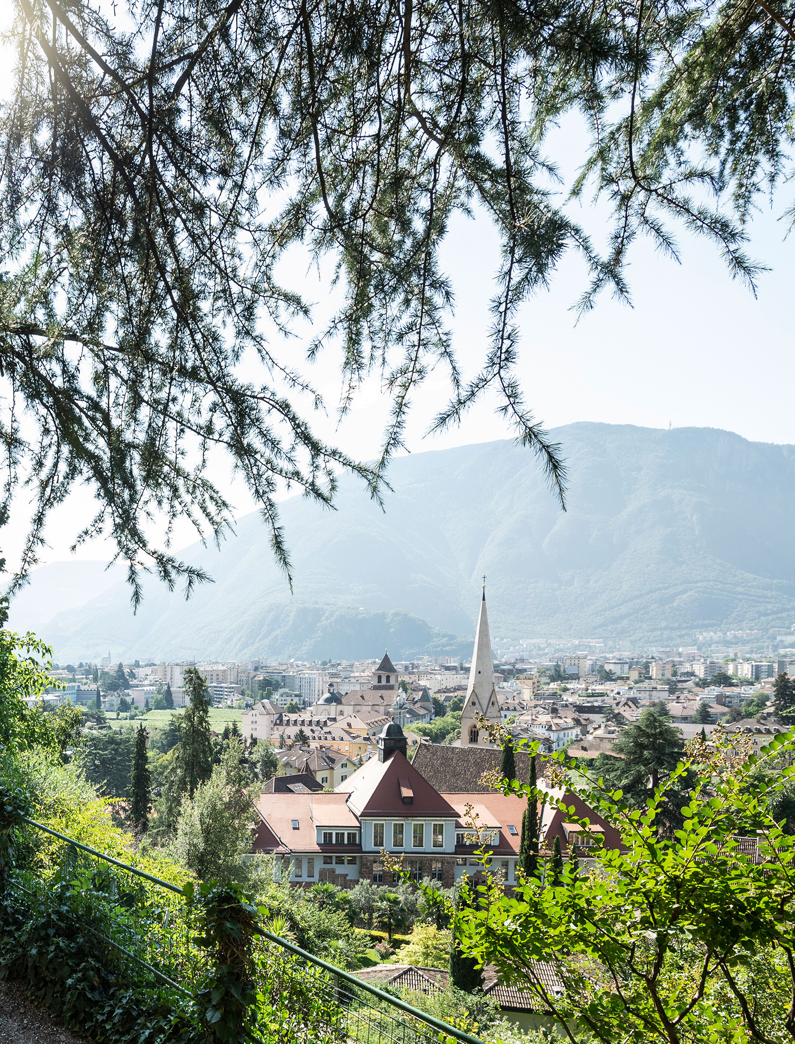 Eine Stadt mit Kirchturm, Gebäuden mit roten Dächern, Bäumen und Bergen im Hintergrund an einem sonnigen Tag. - Hotel Zur Sonne