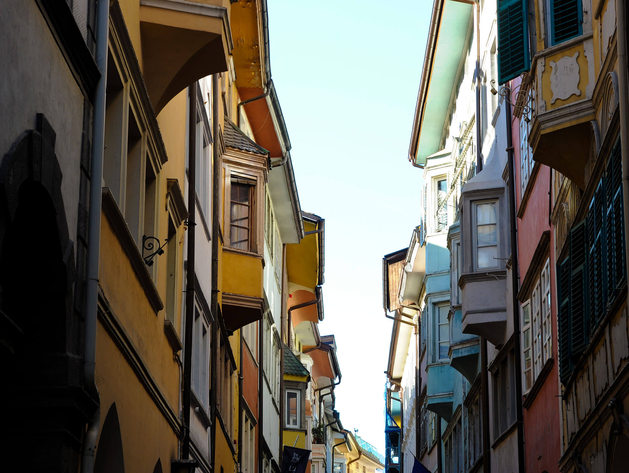 Narrow street with colorful buildings and many windows under a clear sky, viewed from below. - Hotel Zur Sonne