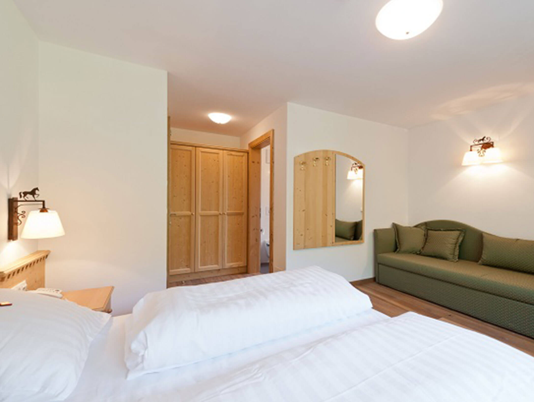Camera d'albergo luminosa con un letto, un divano verde, uno specchio, un armadio in legno e pareti bianche. - Hotel Zur Sonne