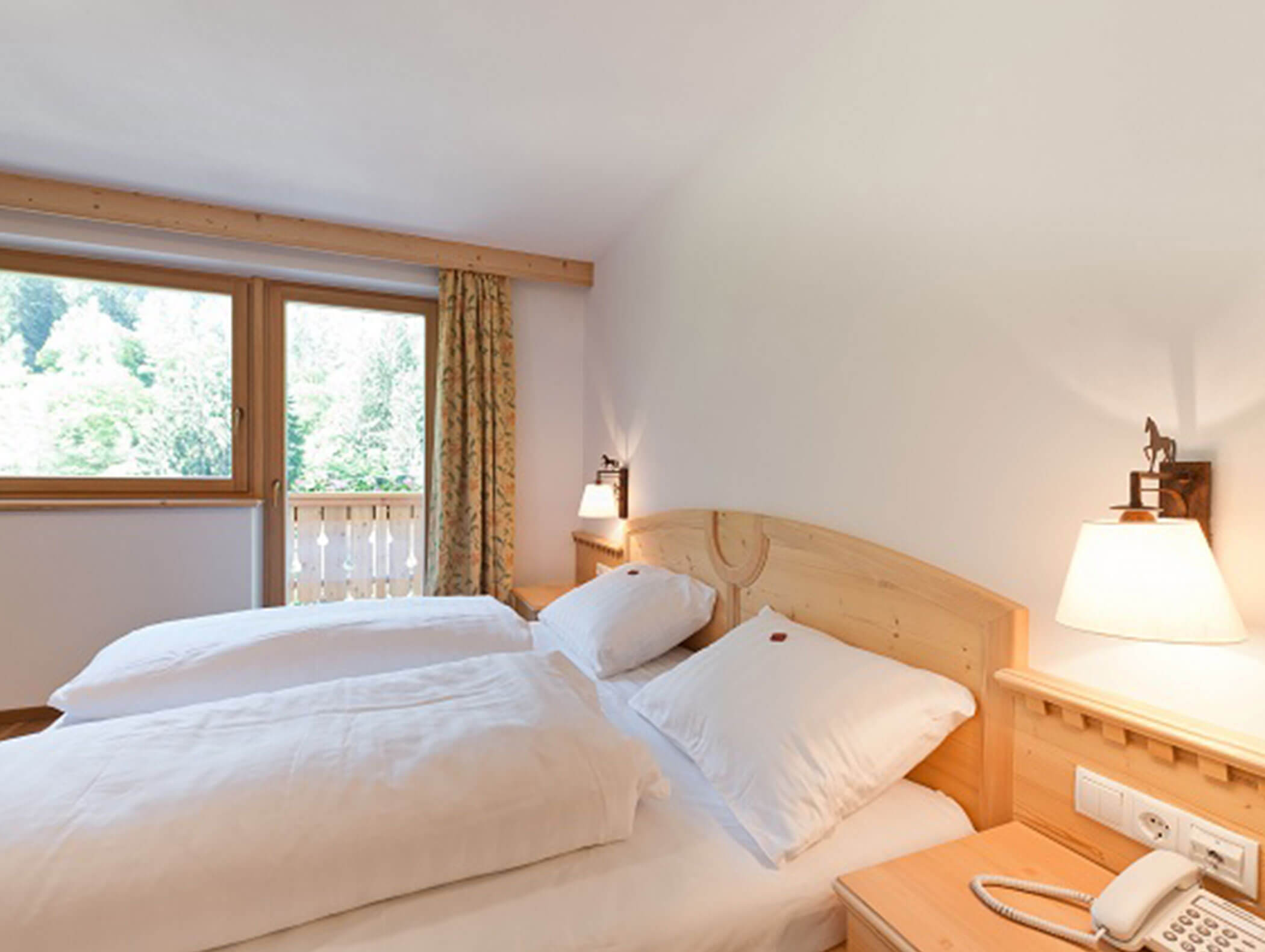 Camera d'albergo luminosa con due letti singoli, mobili in legno, lampade da comodino e una finestra affacciata sul verde. - Hotel Zur Sonne