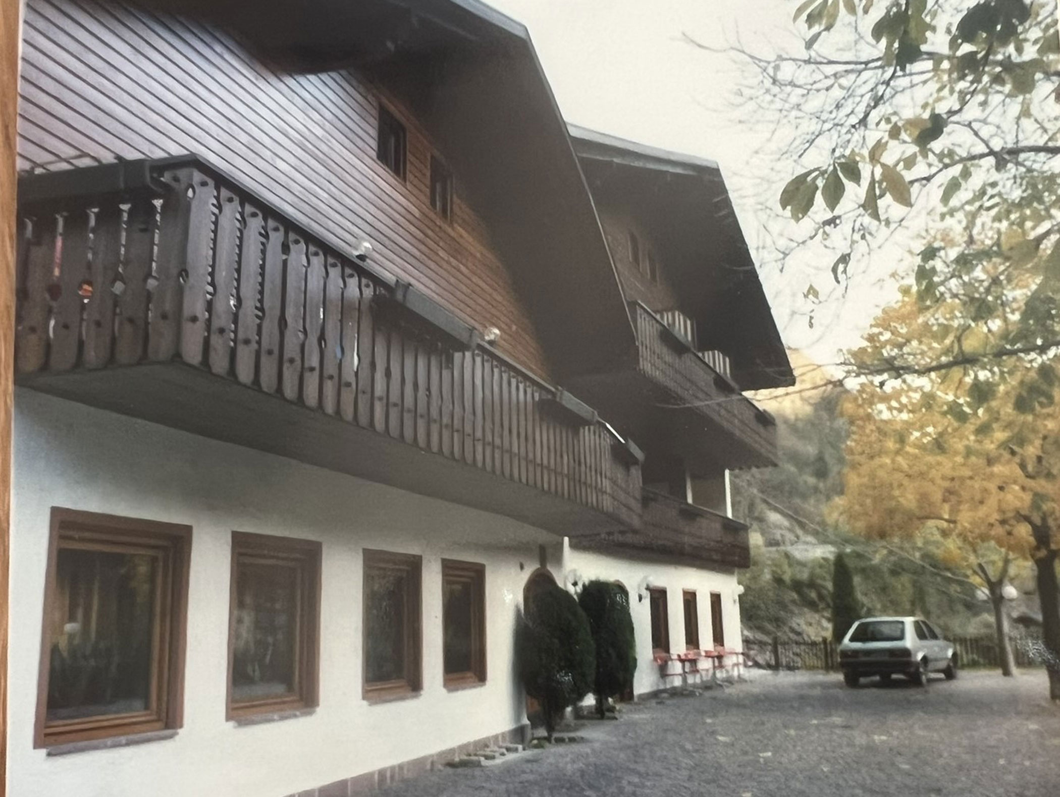 Ein Gebäude im Chalet-Stil aus Holz mit Balkonen, herbstlich gefärbten Bäumen und einem davor geparkten Auto. - Hotel Zur Sonne