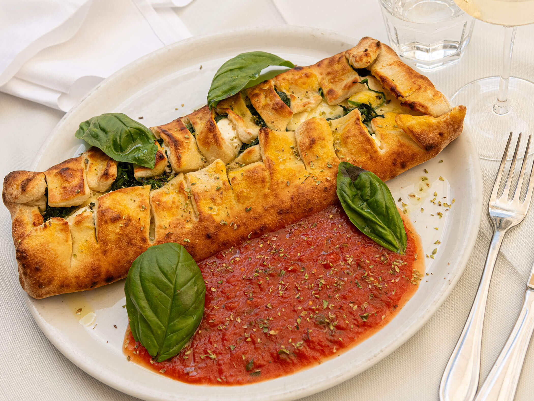 Calzone mit Spinat und Käse, serviert mit Tomatensoße, frischen Basilikumblättern und Kräutern auf einem weißen Teller. - Hotel Zur Sonne