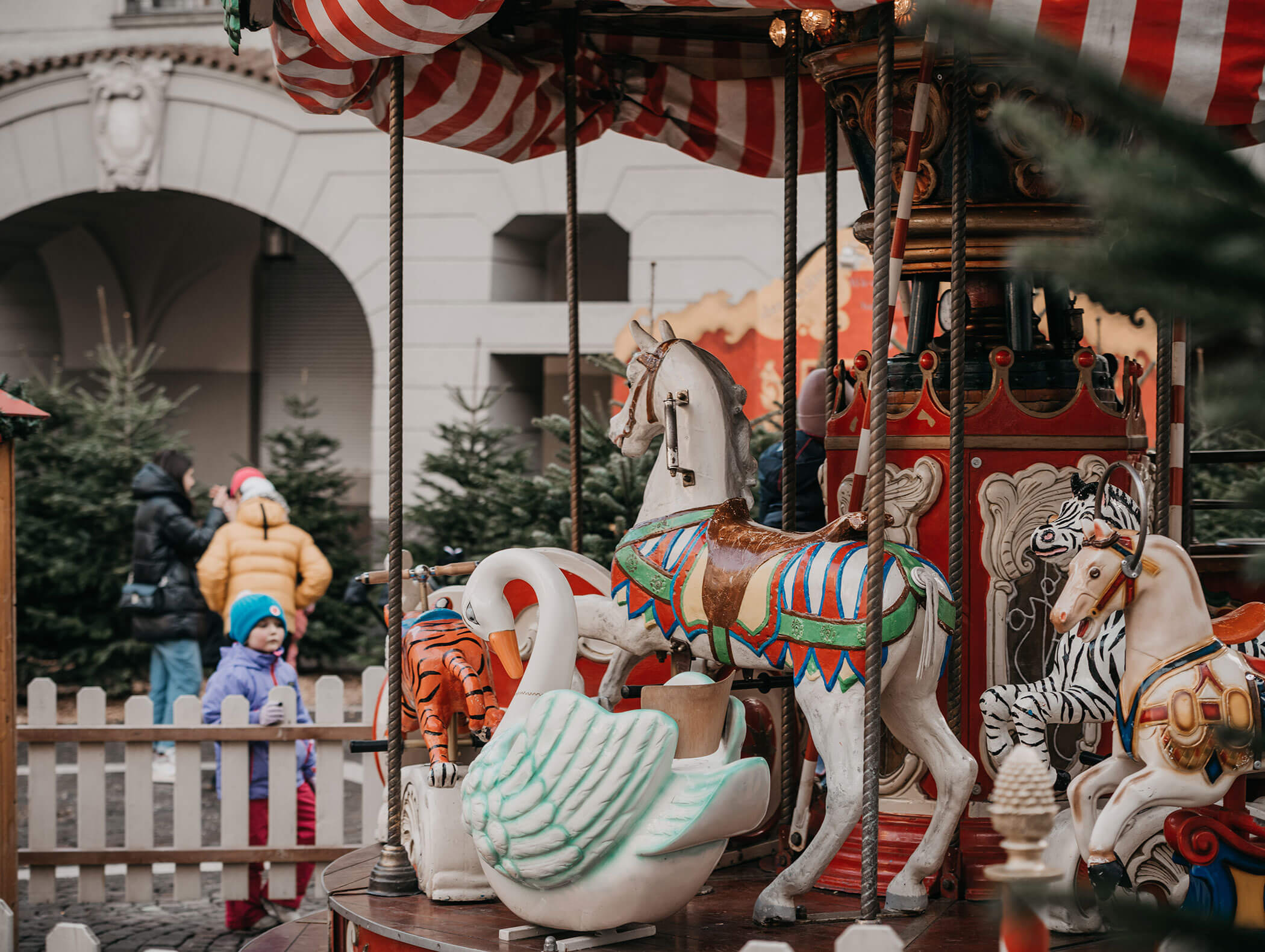 Vintage carousel with horses and a swan; children in winter clothes stand nearby by a white fence. - Hotel Zur Sonne