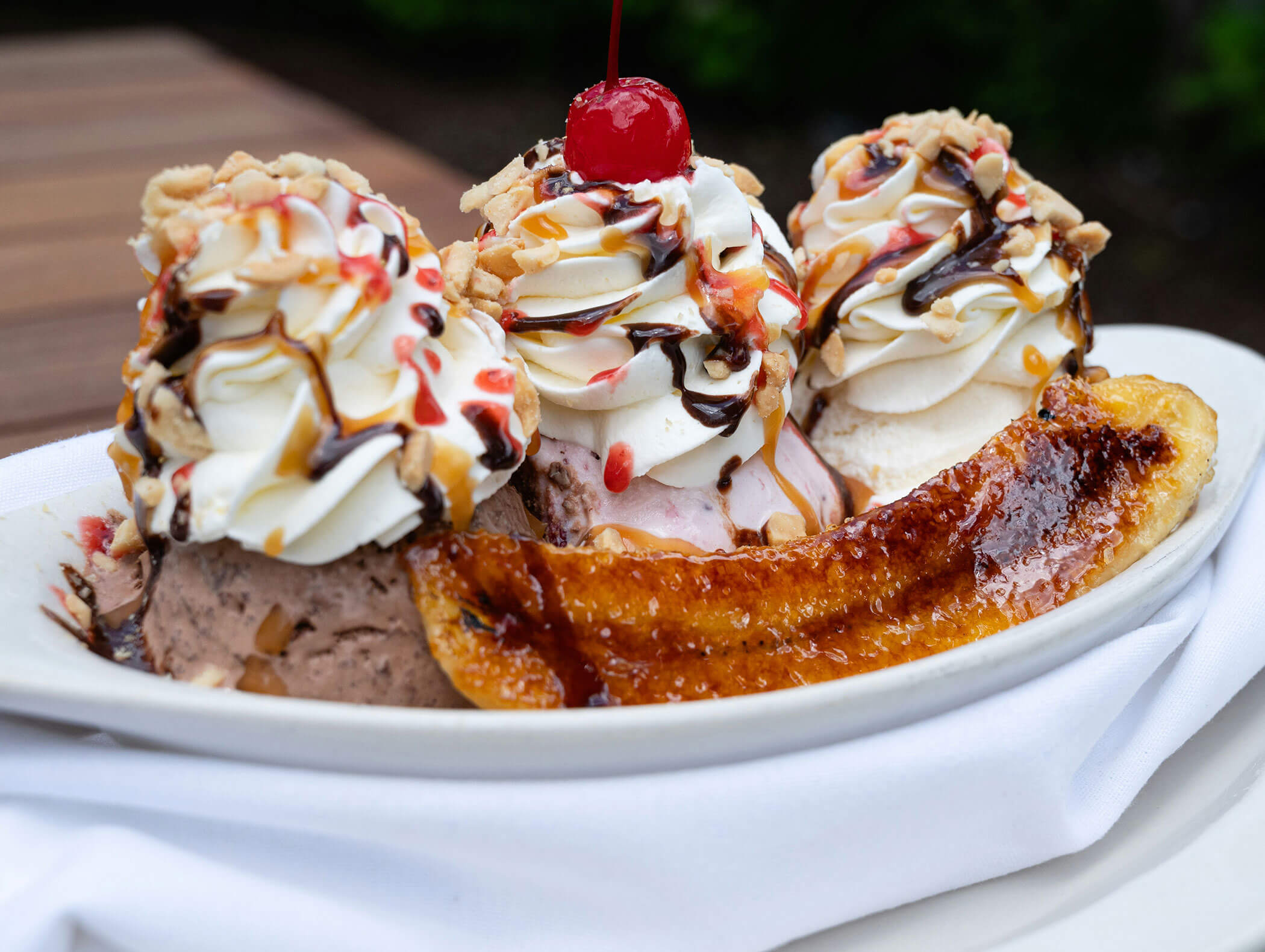 Banana split with whipped cream, chocolate syrup, nuts, and a cherry on top, served on a white plate. - Hotel Zur Sonne
