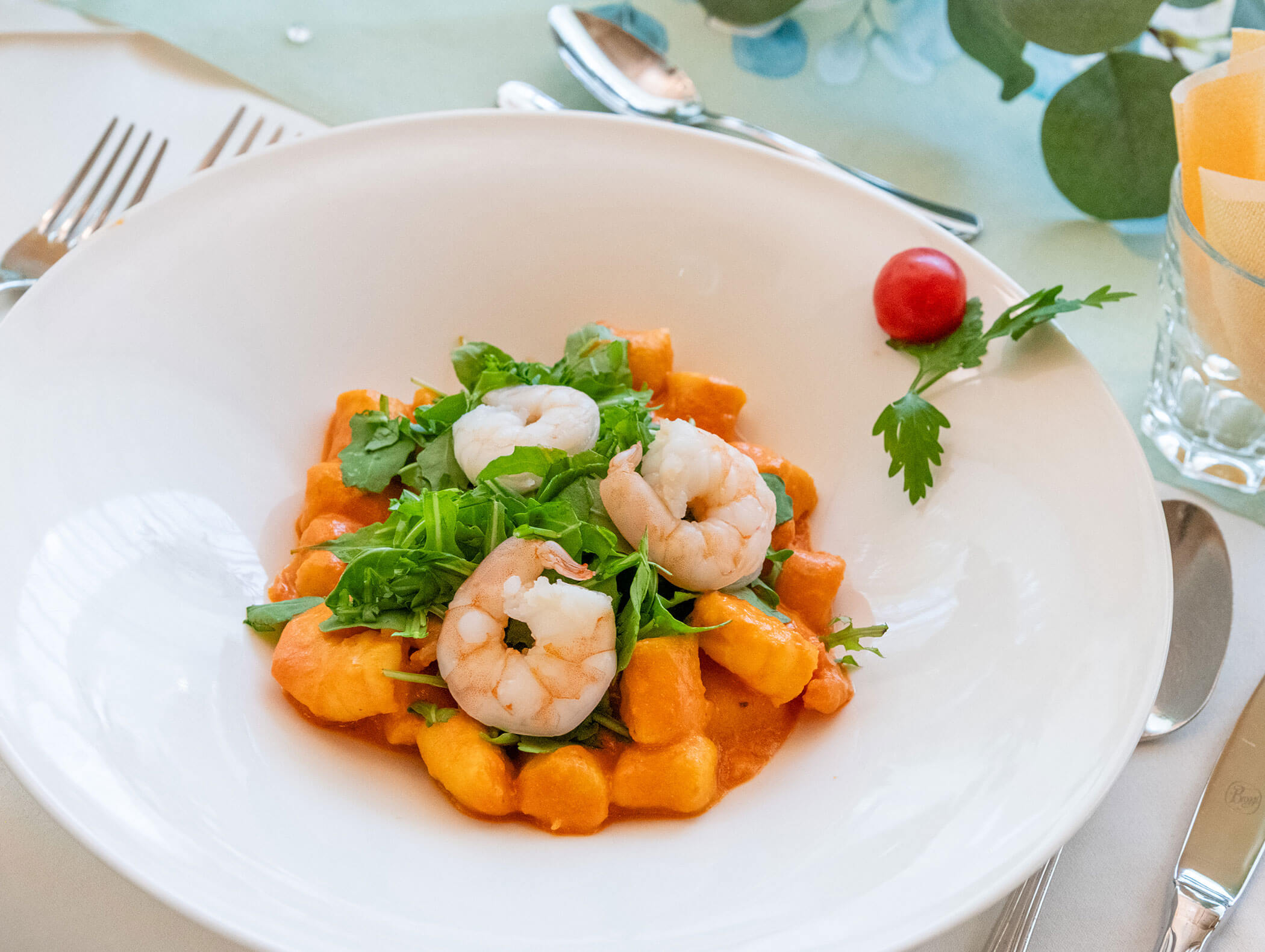 Gnocchi al sugo rosso con gamberetti e rucola, serviti su un piatto bianco con un unico pomodorino. - Hotel Zur Sonne