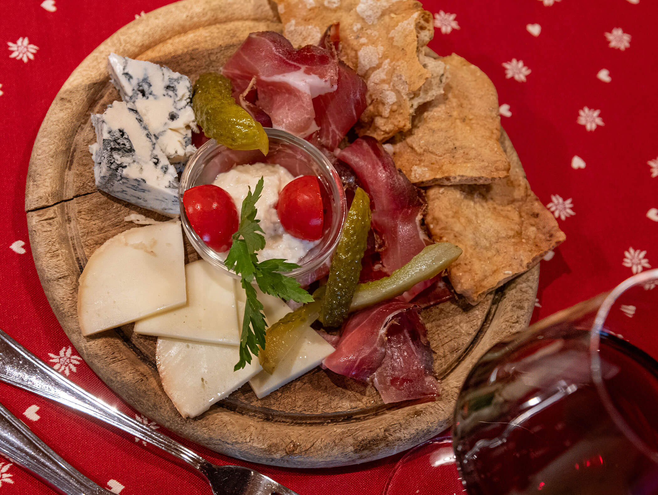 Piatto con un assortimento di formaggi, salumi, pane, sottaceti, pomodori e un bicchiere di vino rosso a corredo. - Hotel Zur Sonne