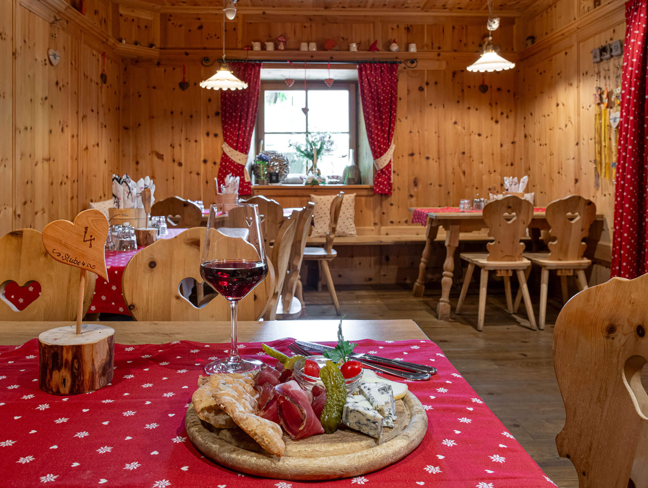 Un bicchiere di vino rosso e un vassoio di salumi e formaggi su un tavolo in un accogliente ristorante con arredi in legno. - Hotel Zur Sonne