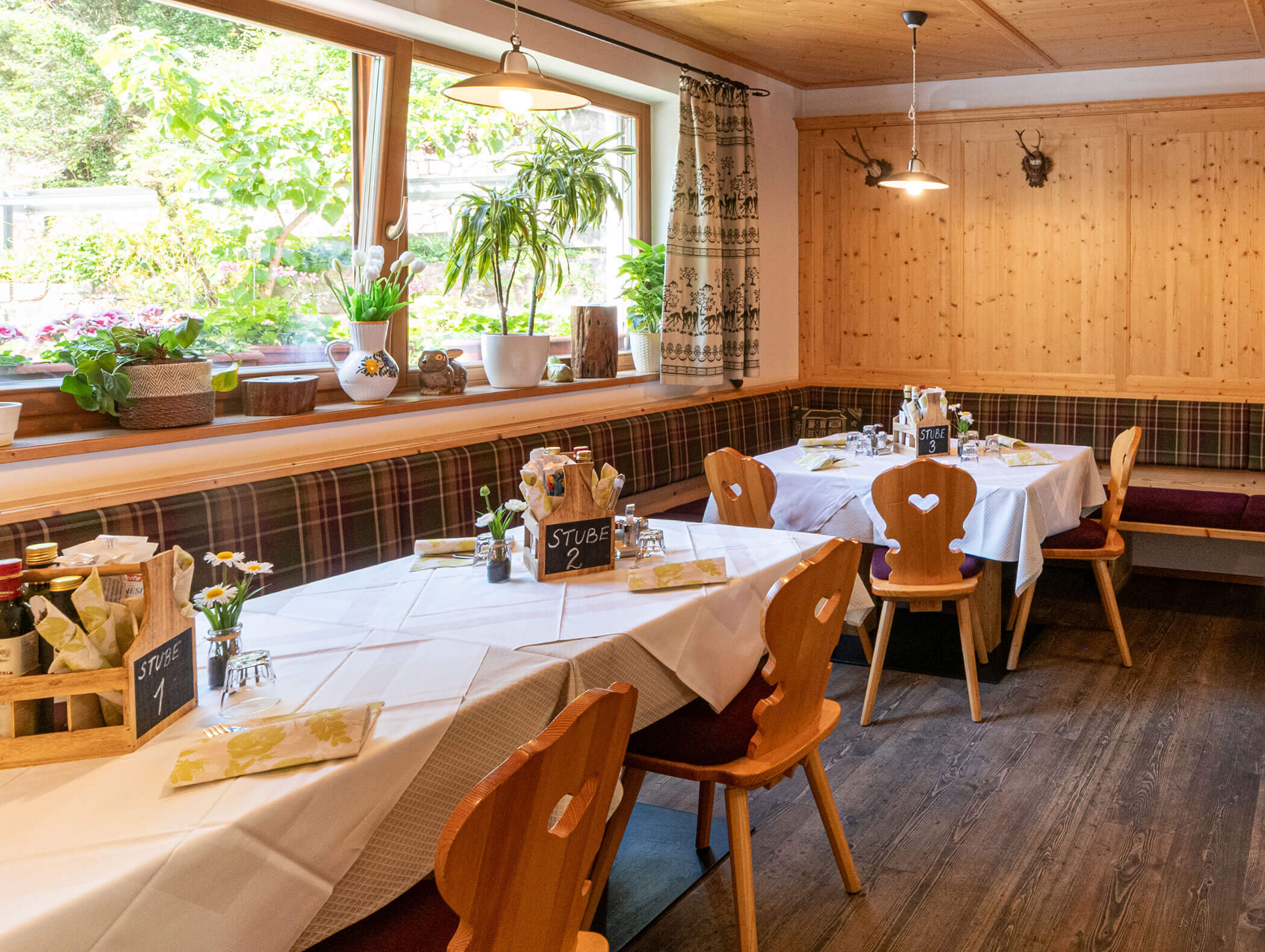 Ristorante accogliente con arredi in legno, tavoli apparecchiati per la cena, un’ampia finestra con piante e luce naturale. - Hotel Zur Sonne
