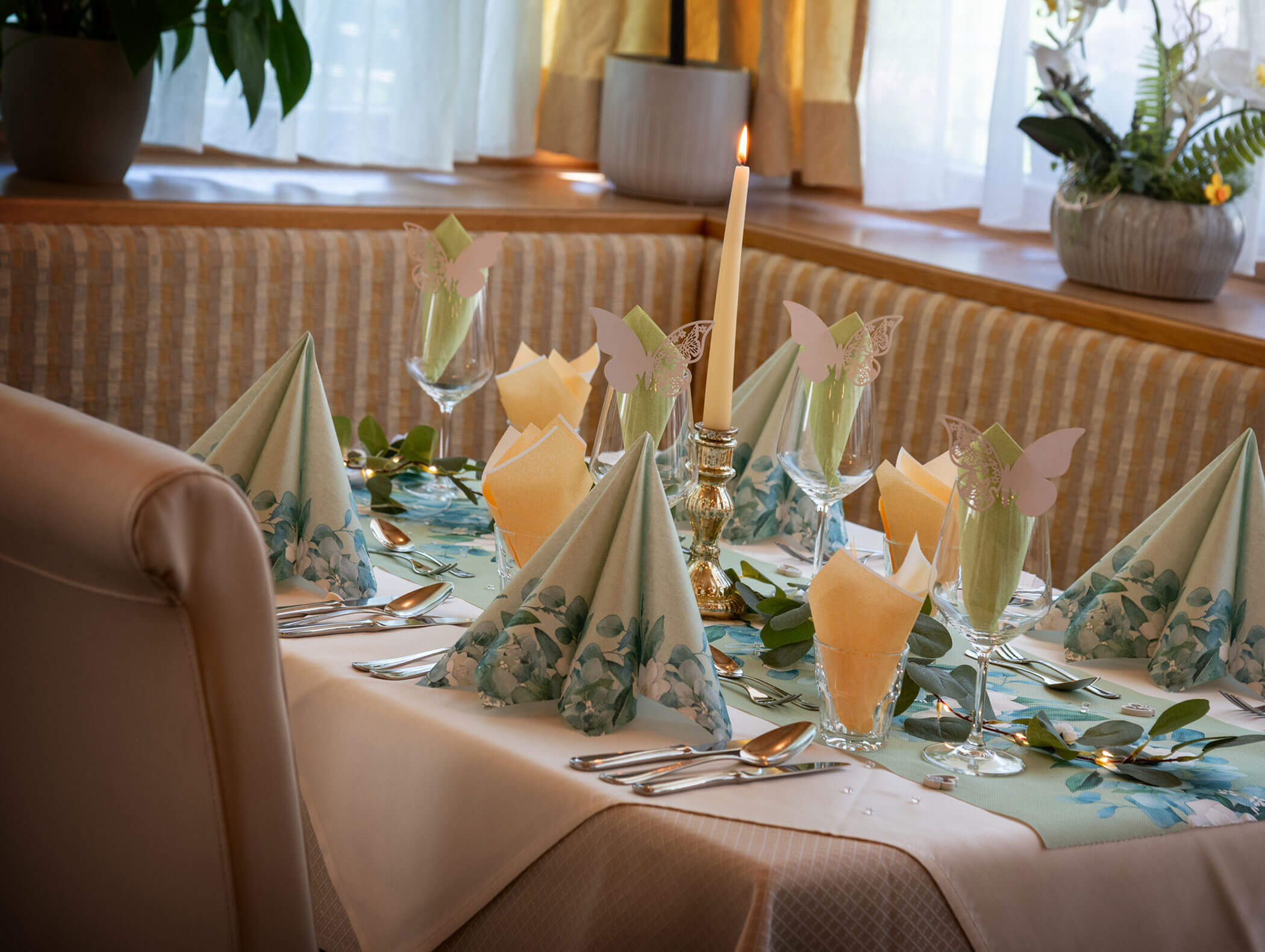 Elegant table set with folded napkins, butterfly decorations, a lit candle, and floral centerpiece. - Hotel Zur Sonne