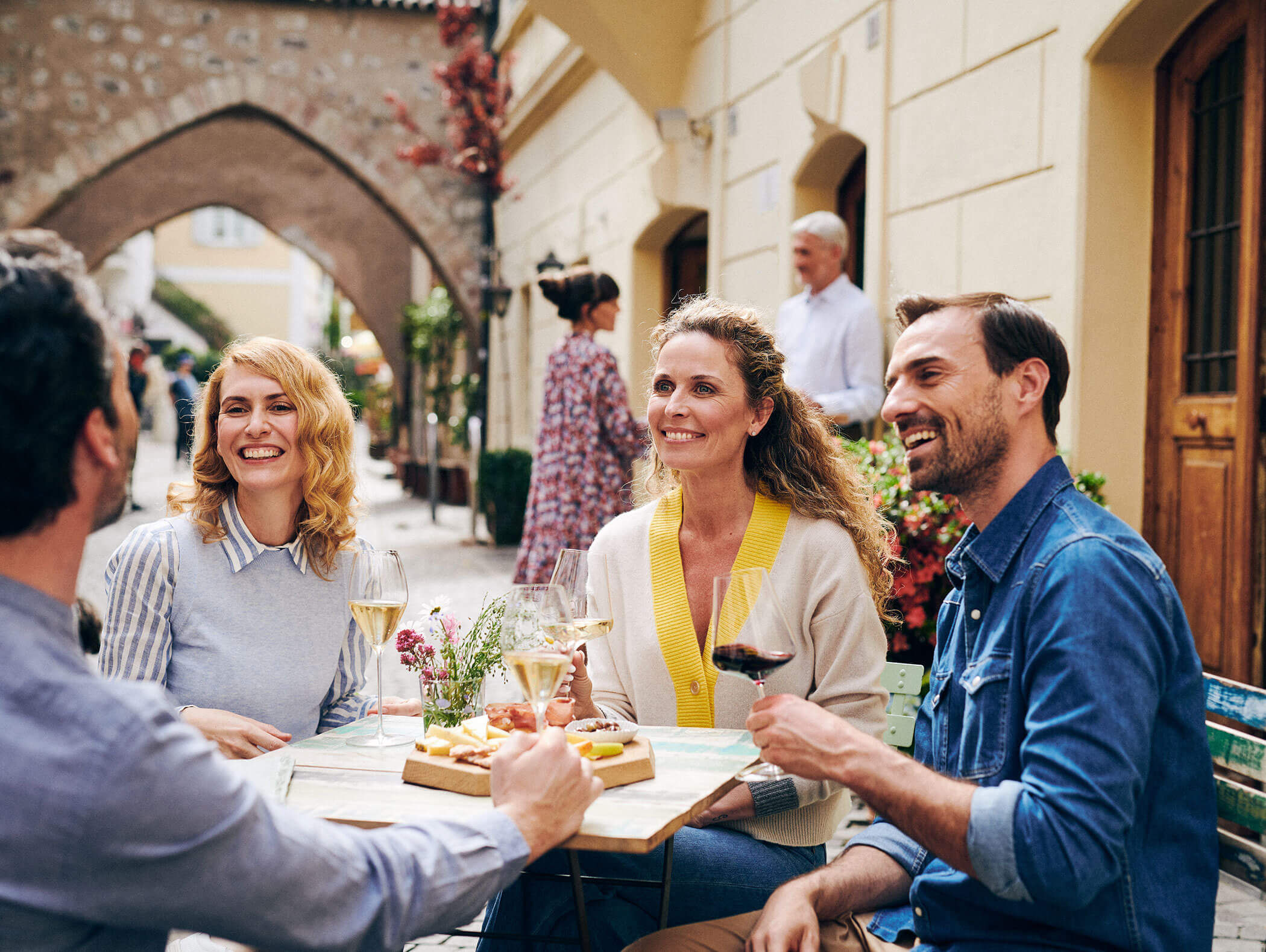 Four people sit outside at a café table, smiling and enjoying drinks and appetizers together. - Hotel Zur Sonne