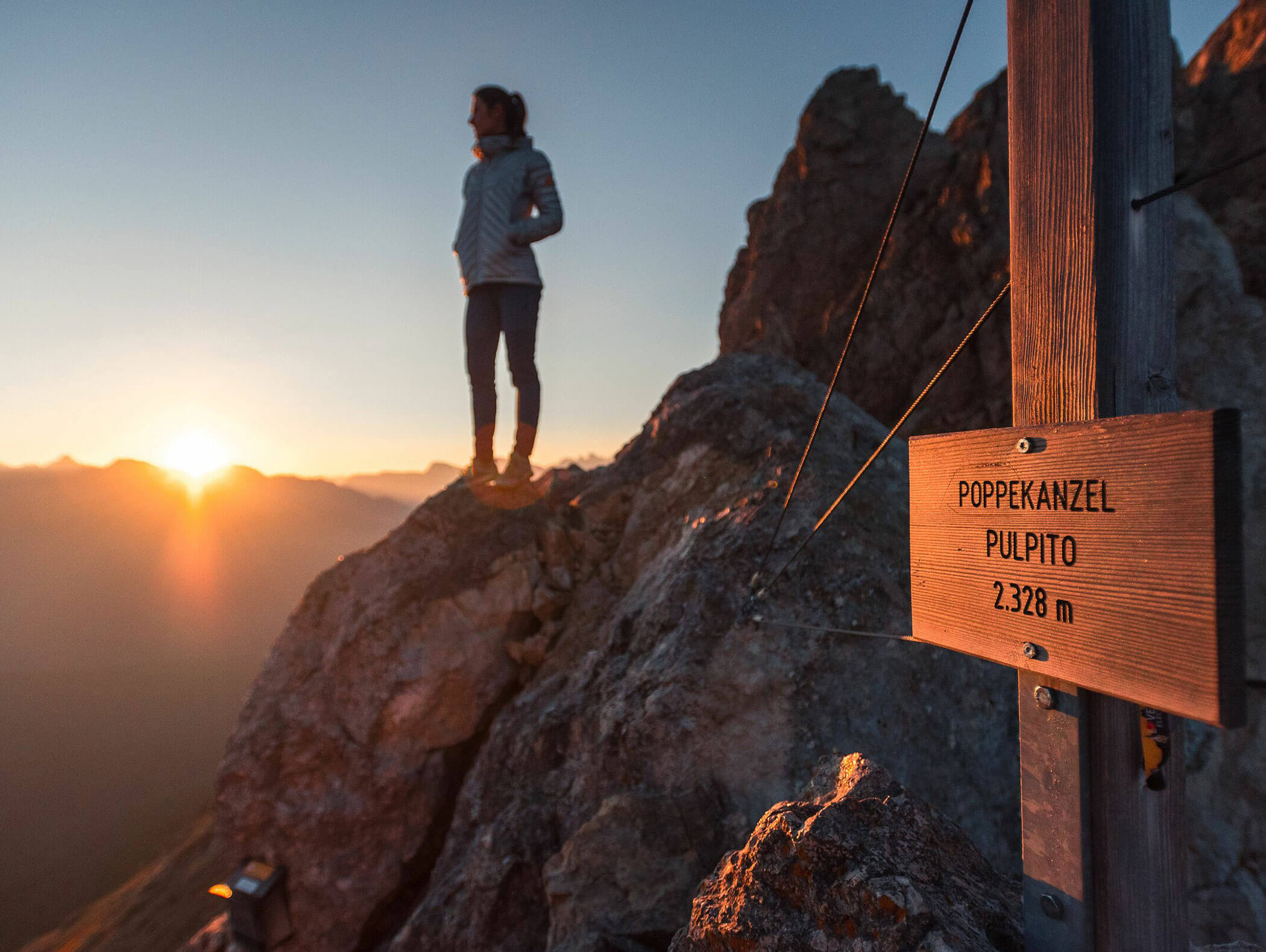Person standing on rocky mountain at sunrise near a sign reading PULPITO 2,378 m.. - Hotel Zur Sonne