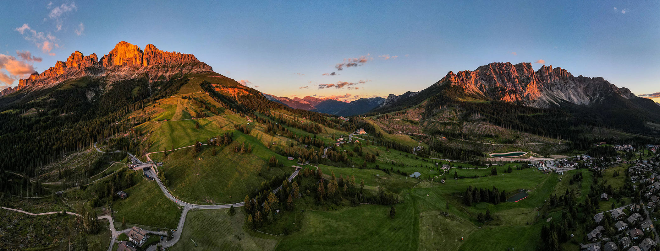 Mountain peaks at sunset with green valleys, winding roads, and scattered houses, under a clear sky. - Hotel Zur Sonne