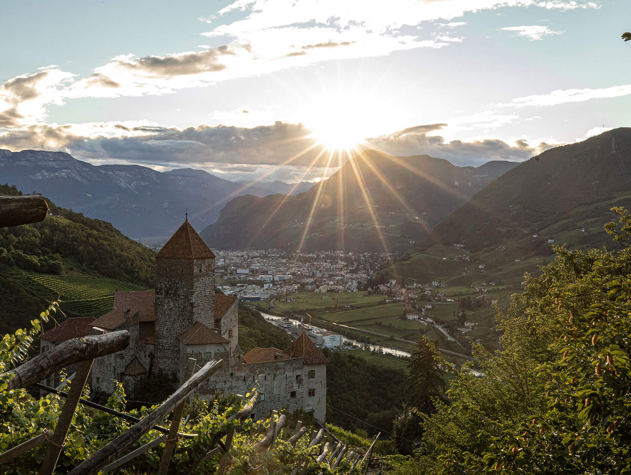 Sun setting over a valley town with a stone castle, mountains, and green hills in the background. - Hotel Zur Sonne