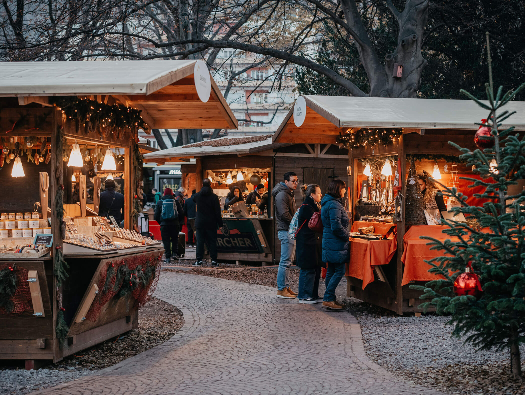 People browsing wooden stalls at a festive outdoor market with lights and holiday decorations. - Hotel Zur Sonne