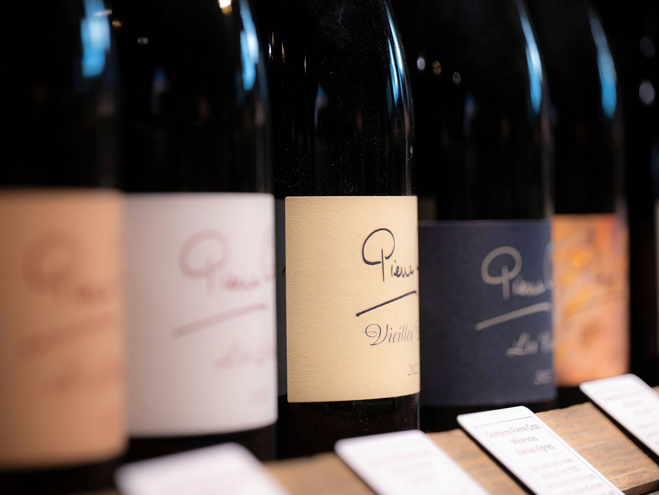 A close-up of several wine bottles with different colored labels lined up on a shelf. - Hotel Zur Sonne