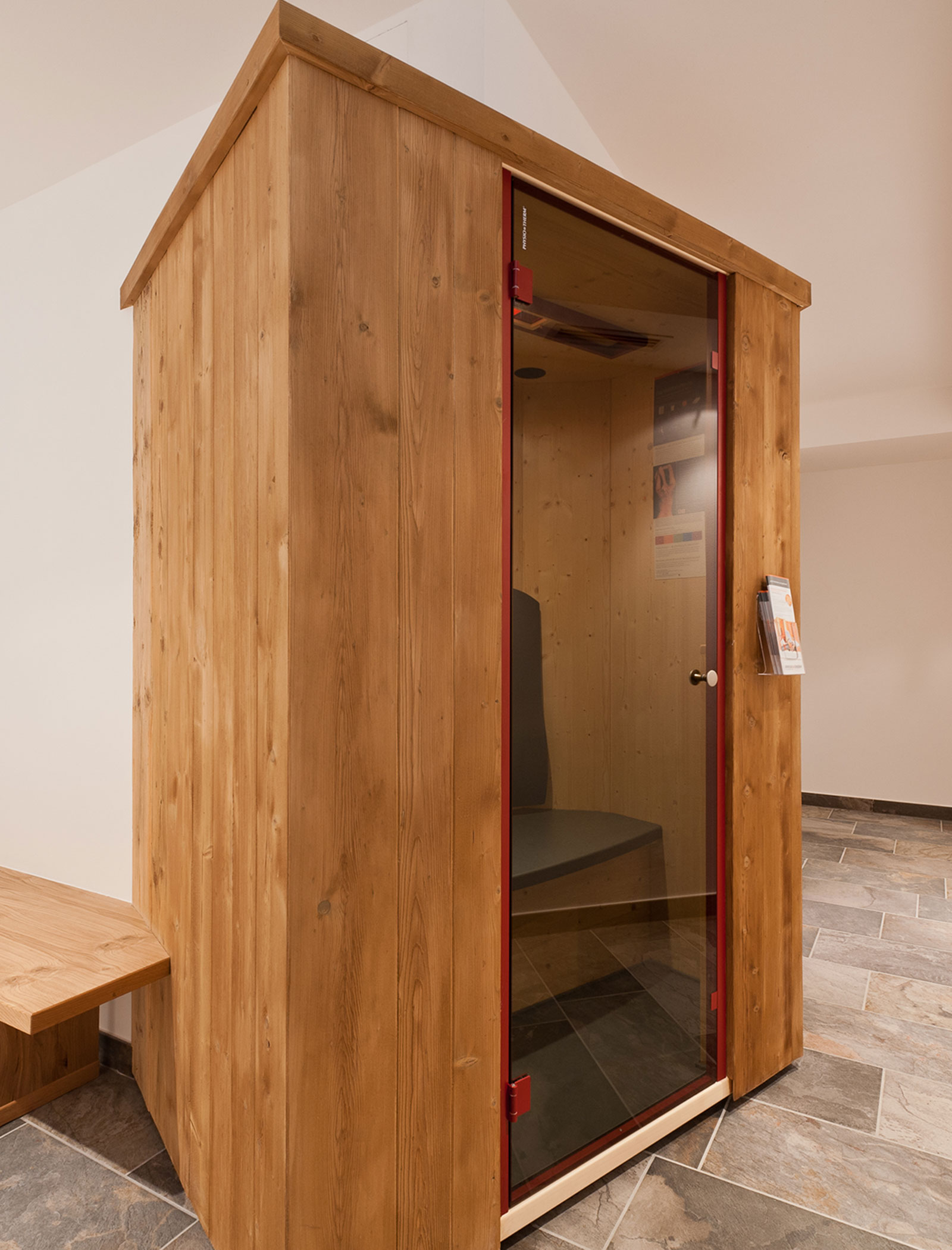 A small wooden sauna with a glass door and a bench inside, set on a tiled floor indoors. - Hotel Zur Sonne