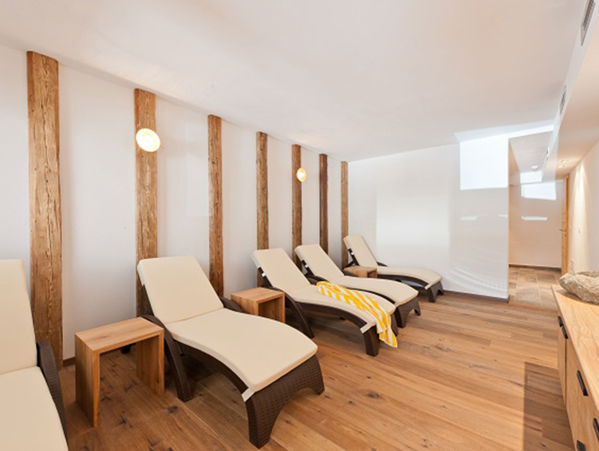 Five beige lounge chairs with wooden side tables in a bright, modern relaxation room with wood flooring. - Hotel Zur Sonne