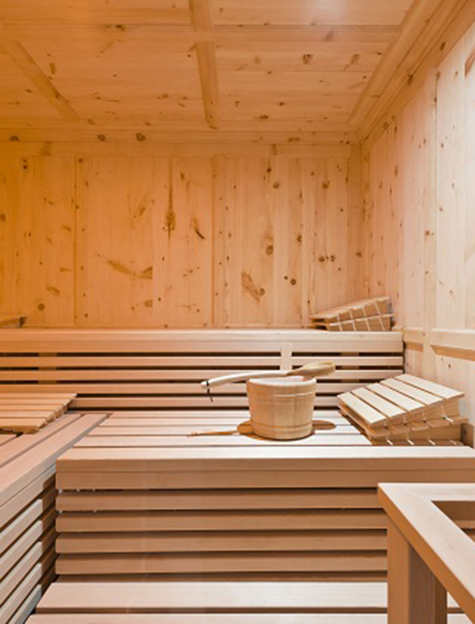Wooden sauna interior with benches, a wooden bucket, and a ladle placed on the bench. - Hotel Zur Sonne