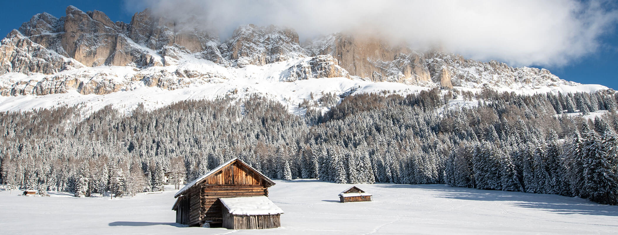 Baite innevate in un prato, pini e alte montagne con le nuvole sullo sfondo. - Hotel Zur Sonne