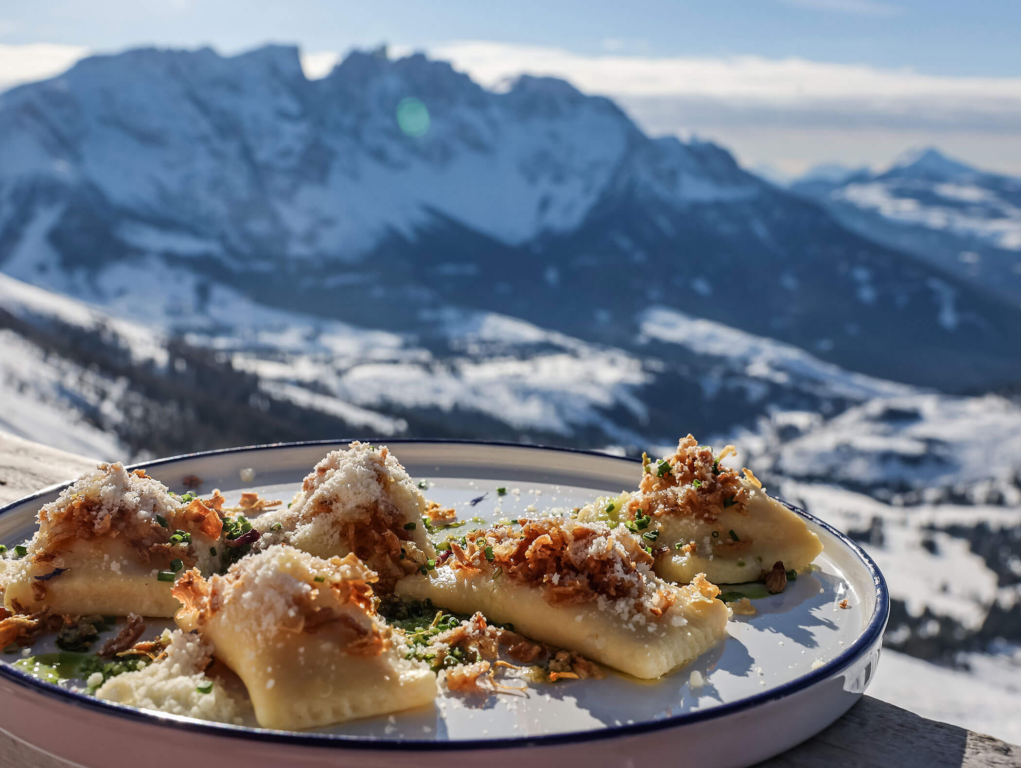 Piatto di pasta ripiena con formaggio ed erbe aromatiche, adagiato su un tavolo con alle spalle le montagne innevate sullo sfondo. - Hotel Zur Sonne
