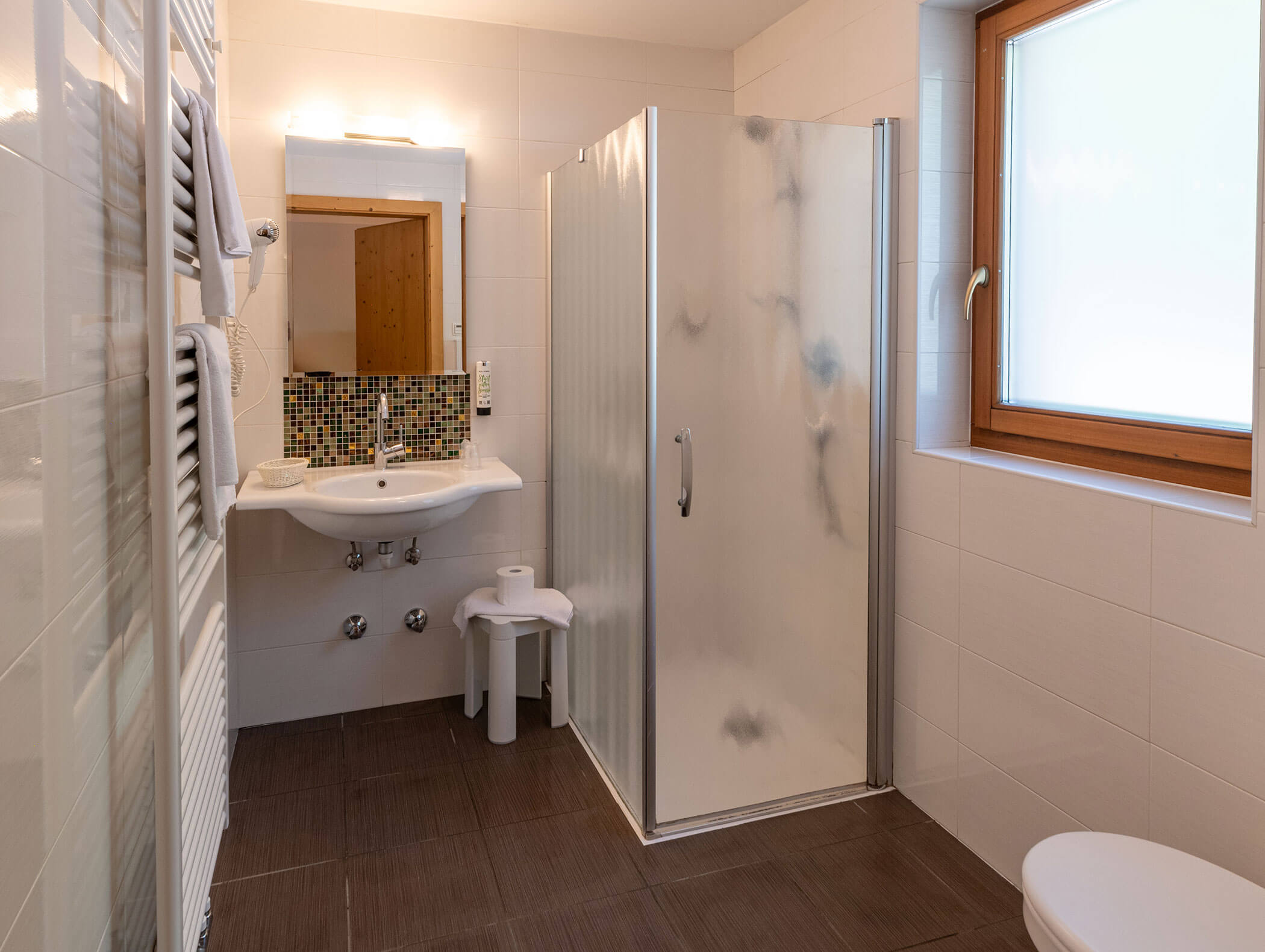 Bagno moderno con box doccia in vetro, lavabo, specchio, WC e finestra che lascia entrare la luce naturale. - Hotel Zur Sonne