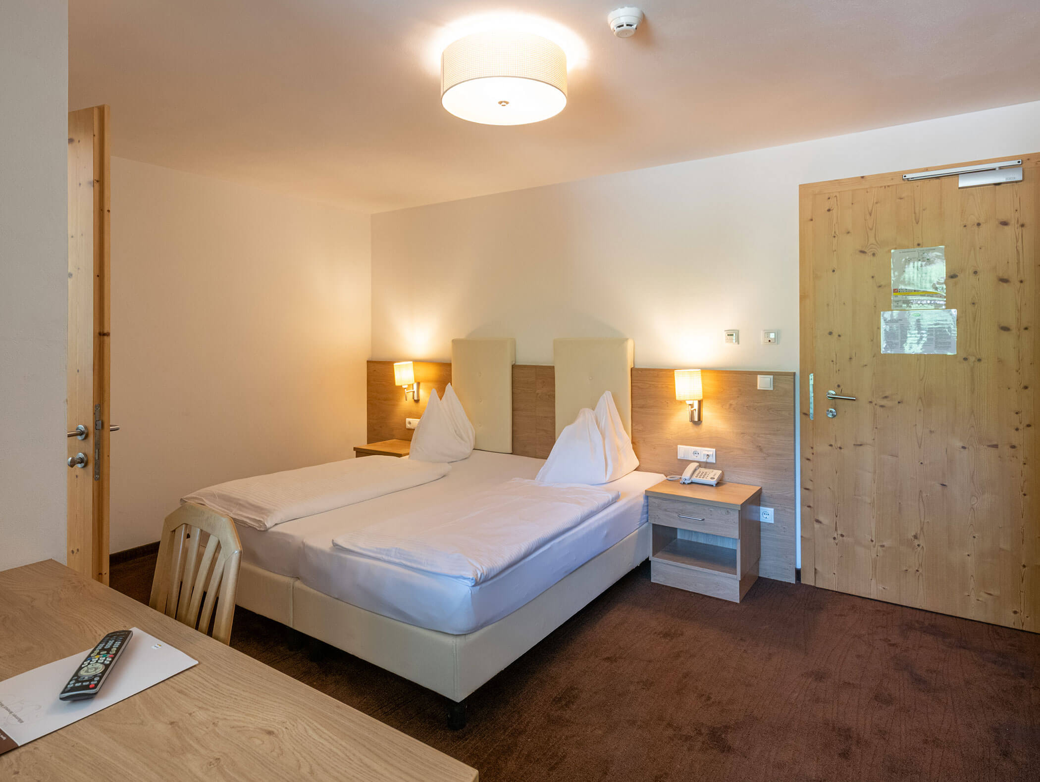 Moderna camera d'albergo con letto matrimoniale, mobili in legno, lampade da parete e una porta in legno chiusa. - Hotel Zur Sonne