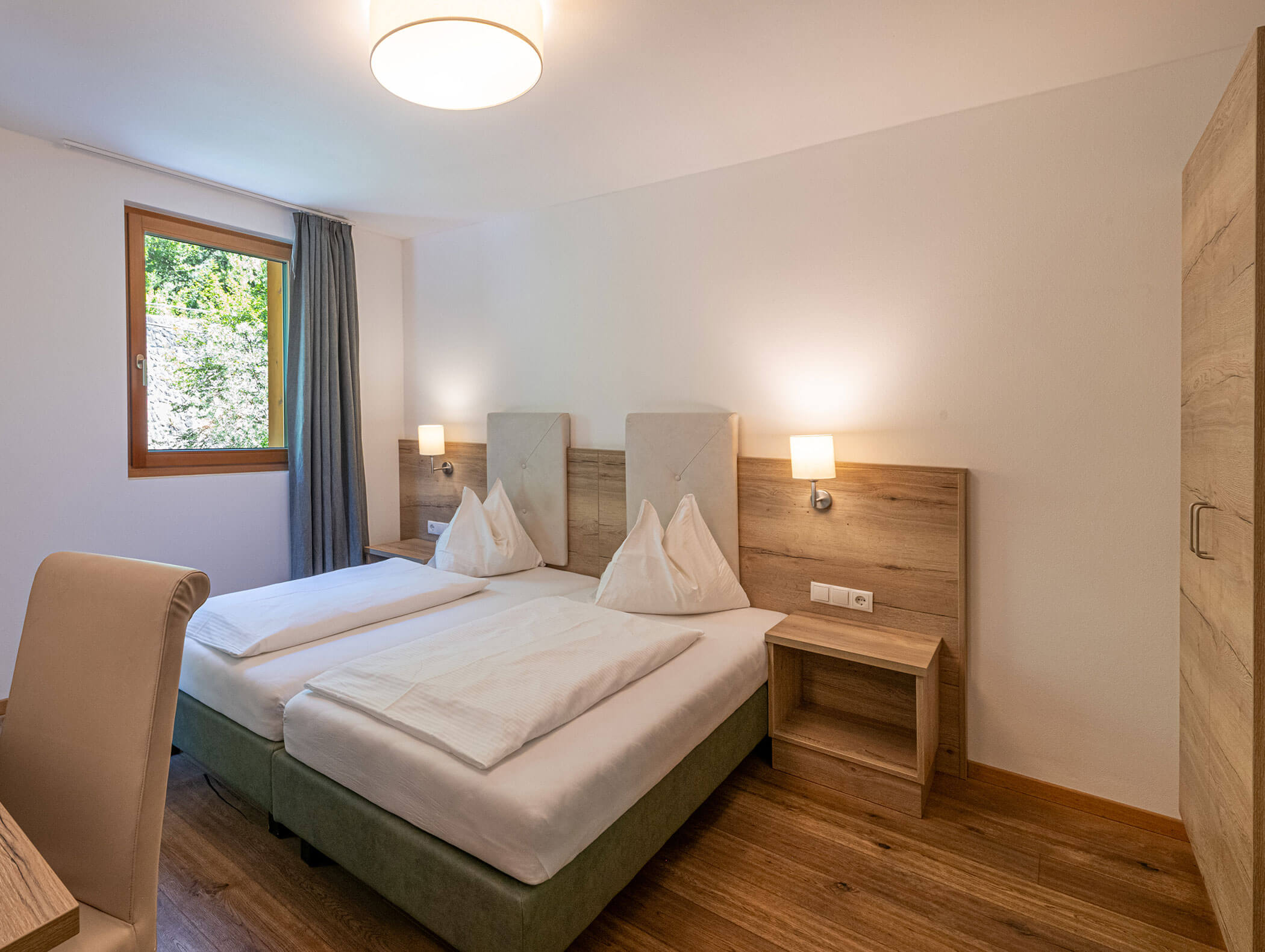 Camera d'albergo moderna con due letti singoli, pavimenti in legno, lampade da comodino e una finestra con tende grigie. - Hotel Zur Sonne