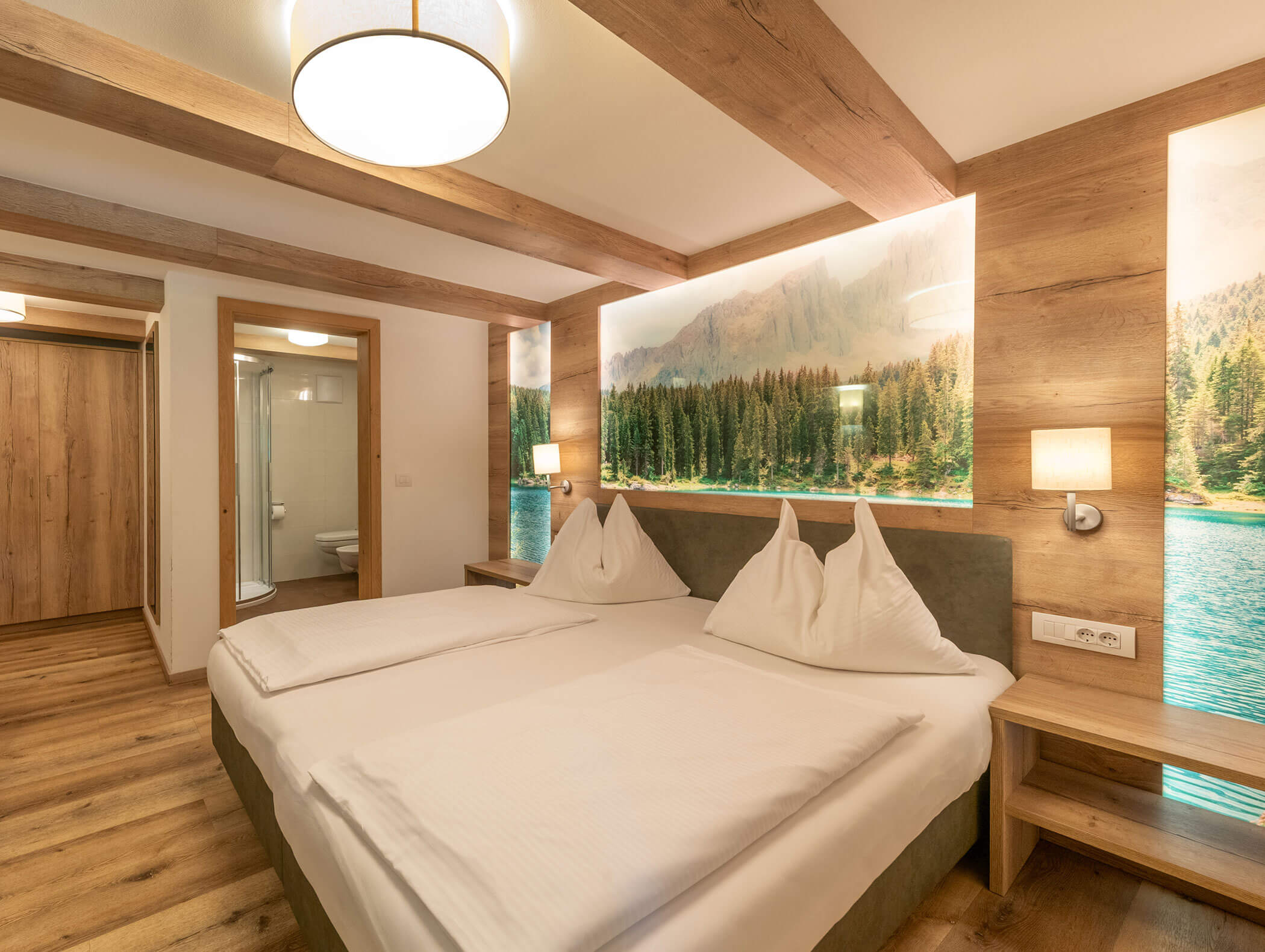 Camera d'albergo moderna con letto matrimoniale, dettagli in legno e un murale raffigurante un lago nel bosco alle spalle del letto. - Hotel Zur Sonne