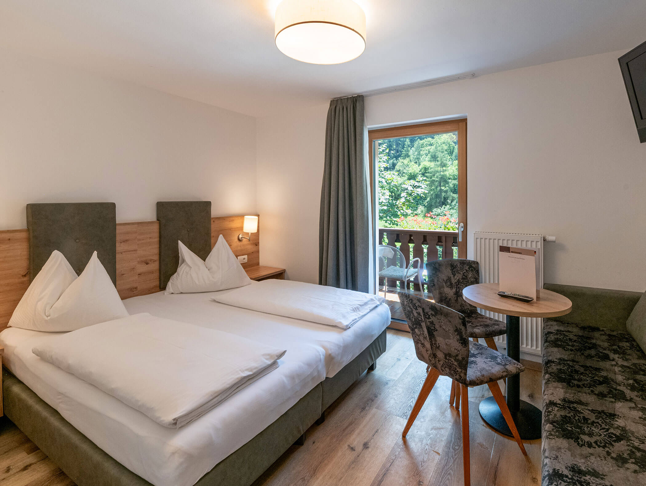 Modernes Hotelzimmer mit Doppelbett, einem kleinen Tisch mit zwei Stühlen und einem Balkon mit Blick ins Freie. - Hotel Zur Sonne