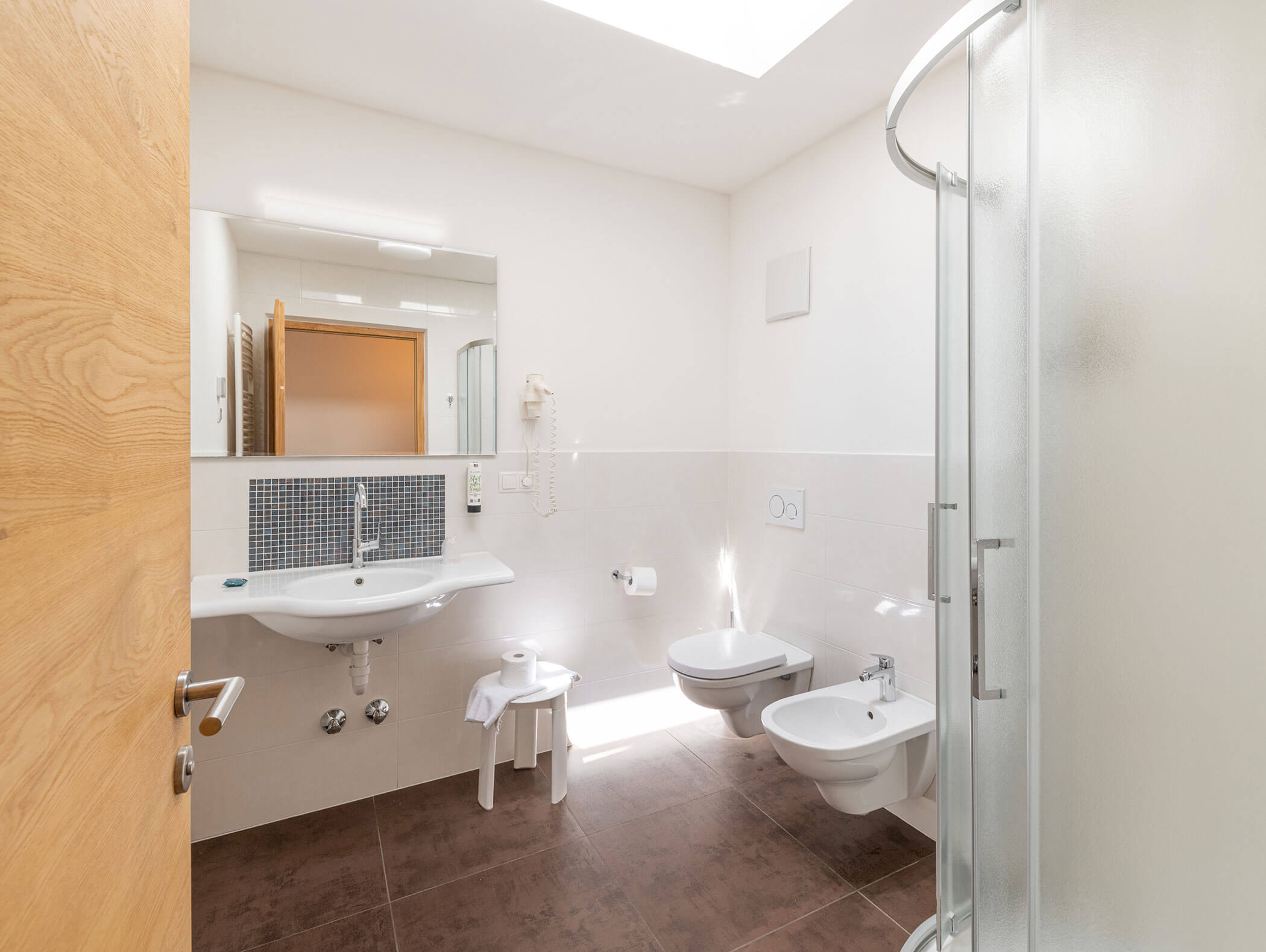 Luminoso bagno con lavabo, WC, bidet e box doccia in vetro curvo, visto dalla porta. - Hotel Zur Sonne