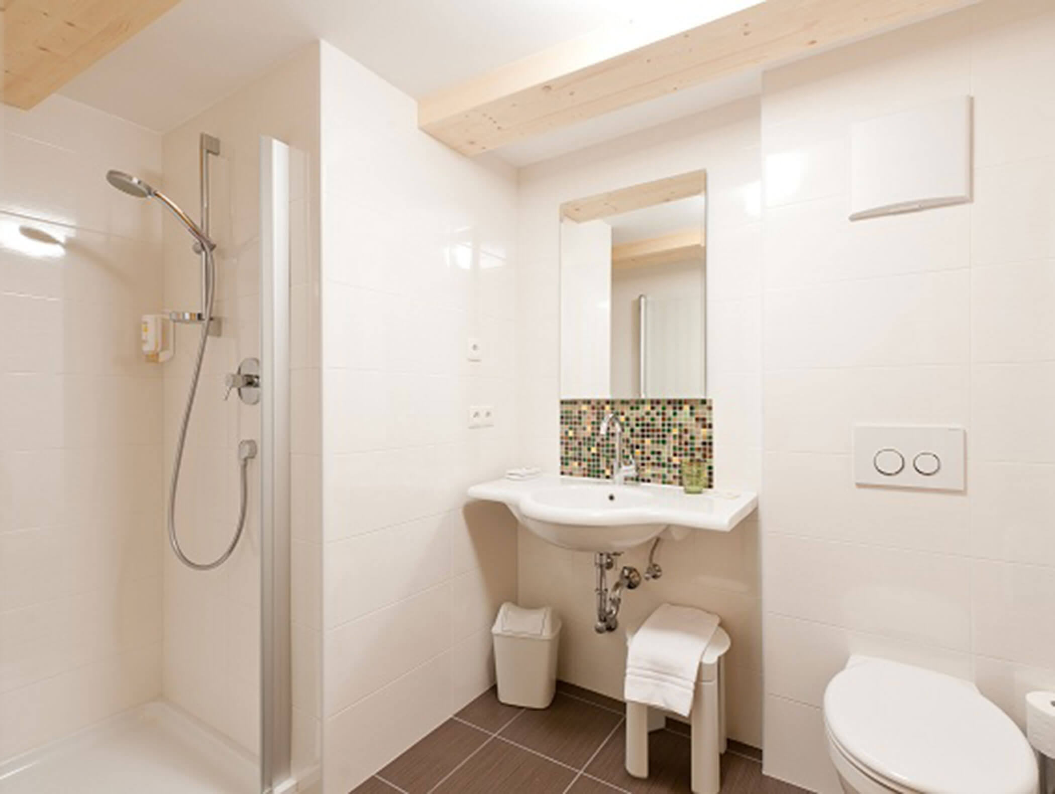 Bagno moderno con cabina doccia, lavabo, specchio, rivestimento in mosaico, WC e cestino dei rifiuti. - Hotel Zur Sonne