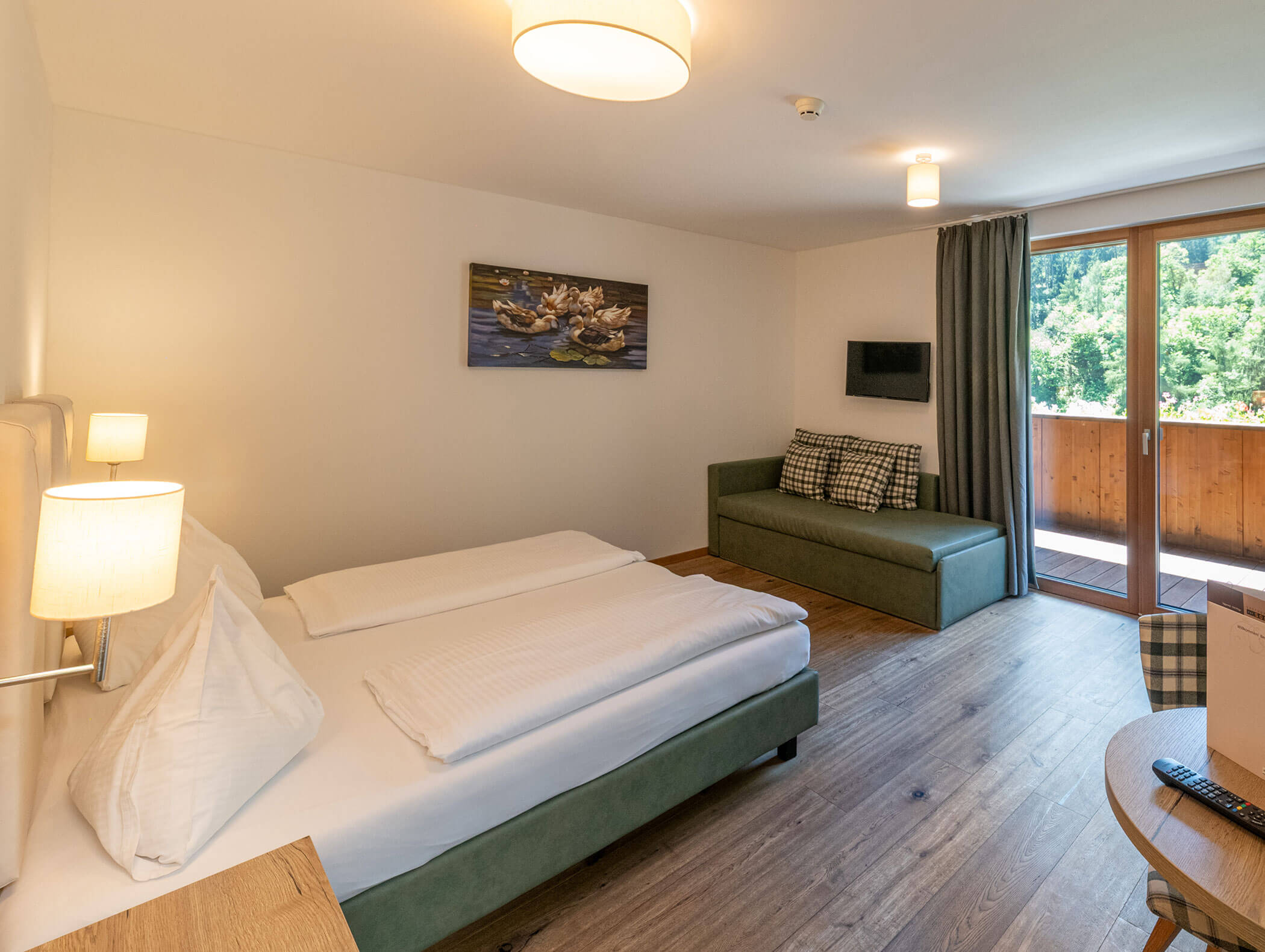 Una camera d'albergo accogliente con letto matrimoniale, divano, quadri alle pareti, porta che dà sul balcone e pavimento in legno. - Hotel Zur Sonne