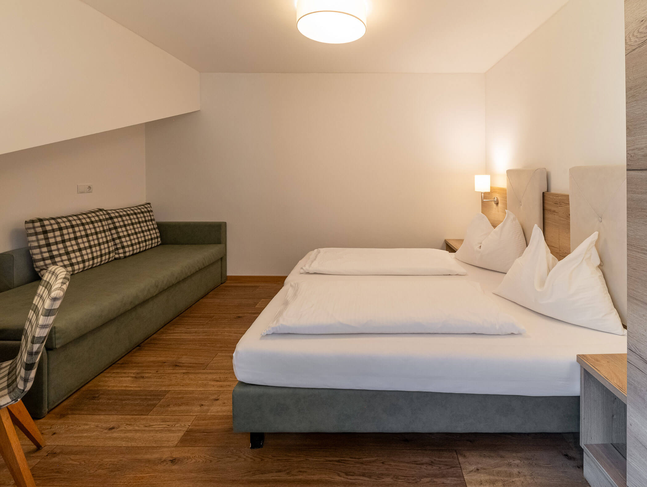 Camera d'albergo moderna con letto matrimoniale, divano, pavimento in legno e illuminazione sobria. - Hotel Zur Sonne