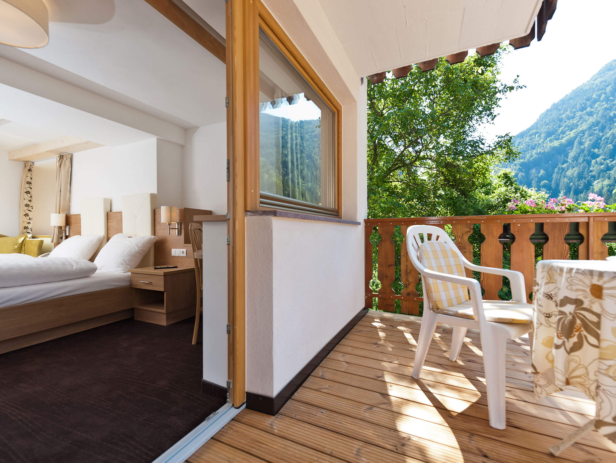 Un'accogliente camera d'albergo si affaccia su un balcone in legno con una sedia, un tavolo e vista sulle montagne. - Hotel Zur Sonne