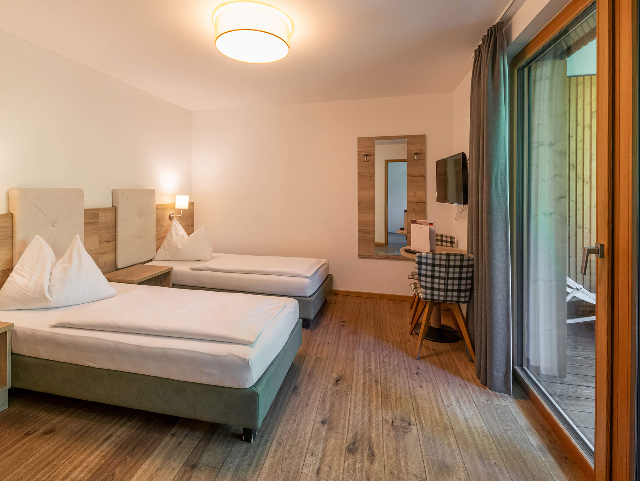 Moderna camera d'albergo con due letti singoli, una scrivania, una TV a parete e una porta a vetri che dà sul balcone. - Hotel Zur Sonne