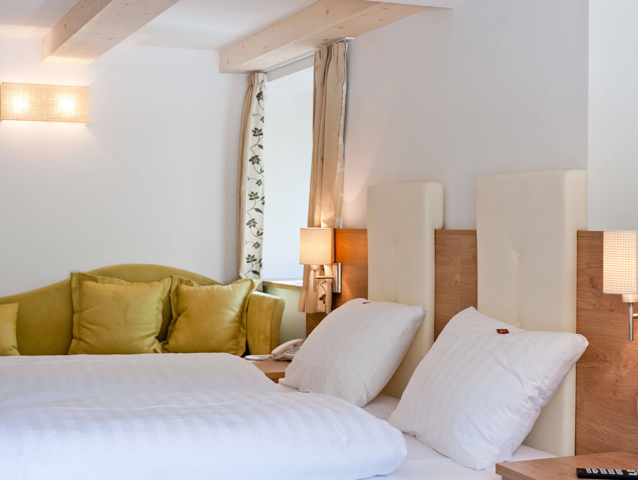 Un letto ben rifatto con lenzuola bianche, un divano verde e luci soffuse in una stanza accogliente e moderna. - Hotel Zur Sonne